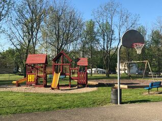 A sliver of the basketball court with the playground and swing set behind it. Trees are visible behind the swing set.